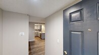 Located at 2800 Madison Avenue in Fullerton, California, this single-story unit offers a thoughtfully updated interior with a cohesive, modern aesthetic throughout. Dark wood-look vinyl plank flooring flows consistently across the living areas and bedrooms, anchoring the neutral warm-gray color palette that defines the space.

The kitchen serves as a functional centerpiece, featuring gray shaker-style cabinetry, stone-look quartz countertops, a mosaic tile backsplash, and stainless steel appliances including a refrigerator. A dedicated built-in cabinet nook adjacent to the kitchen provides additional storage and display space, while recessed ceiling lighting enhances visibility. Entry into the unit is marked by a distinctive deep-blue front door.

The living area is generously proportioned with a ceiling fan and a sliding glass door that opens to an outdoor patio, bringing in natural light and exterior views of landscaping. Bedrooms feature the same wood-look flooring, textured ceilings, and access to natural light through windows.

Two bathrooms offer updated finishes, including gray vanities with white countertops. One bathroom includes a tub-shower combination, while the second features a walk-in shower with sliding glass doors. An additional utility/garage space with a concrete floor and electrical panel provides practical storage or parking.