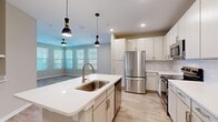This single-story home offers a thoughtfully designed layout across a comfortable footprint, accommodating three bedrooms, two bathrooms, and a dedicated laundry room. The open-concept kitchen and living area serves as the heart of the home, featuring light wood-look flooring, recessed lighting, and stylish pendant lights over a central island with a white quartz countertop and undermount sink with a brass-finish faucet. The kitchen is well-equipped with white shaker-style cabinetry extending to the ceiling, white subway tile backsplash, stainless steel appliances including a refrigerator, range, microwave, and dishwasher. The living area benefits from multiple large windows with white blinds, allowing generous natural light, and includes a ceiling fan. Bedrooms feature neutral-toned carpet flooring and windows providing outdoor views. The primary bedroom is a comfortable size with its own closet. The bathrooms include wood-look tile flooring, white quartz vanity countertops, and a tiled tub-shower combination. A dedicated laundry room houses a full-size washer and dryer with overhead wire shelving. Three closets throughout provide ample storage.
