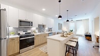 Located at 2960 Tutt Blvd in Colorado Springs, CO, this thoughtfully designed one-bedroom, one-bathroom residence offers a cohesive modern aesthetic across its single floor. The open-concept kitchen and living area serves as the heart of the home, featuring a generous white quartz island with seating, two-tone cabinetry combining crisp white upper cabinets with warm natural wood lower cabinets, and a textured gray tile backsplash. Stainless steel appliances — including a gas range, over-the-range microwave, dishwasher, and refrigerator — complete the kitchen. Pendant lighting above the island and recessed ceiling lights provide layered illumination throughout. Light wood-style flooring runs continuously through the main living areas, adding warmth and visual flow. The living room is bright and inviting, highlighted by a ceiling fan, large windows, and a glass-paneled door that fills the space with natural light. The bedroom offers a comfortable retreat with plush carpeting, a ceiling fan, and a sizable window. The bathroom features a walk-in glass-enclosed shower, white cabinetry with a quartz countertop, and wood-style flooring. Clean lines, neutral tones, and modern hardware unify the design throughout the entire residence.