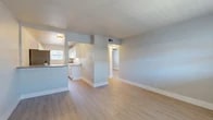 Located at 1600 E Belt Line Rd in Carrollton, TX, this 2-bedroom, 1-bathroom unit offers a clean, modern aesthetic throughout its efficiently designed single-floor layout. Light wood-style flooring runs continuously through the living areas, kitchen, hallway, and both bedrooms, creating a cohesive and bright atmosphere. The open living room flows naturally toward the kitchen, which is separated by a half-wall partition. The kitchen is well-appointed with white cabinetry, granite-style countertops, stainless steel appliances including a full-size refrigerator and electric range, and a window that brings in natural light. Both bedrooms feature the same light wood flooring, ceiling fans, and windows with blinds that allow for natural views of the surrounding greenery. The primary bedroom includes a closet and additional storage. The hallway connects the living area to the bedrooms and bathroom, maintaining a practical flow throughout. The bathroom is highlighted by a full soaking tub surrounded by elegant large-format marble-look tile, giving the space a refined, updated feel. Neutral gray walls and white trim throughout lend a fresh, move-in-ready appearance to the entire unit.