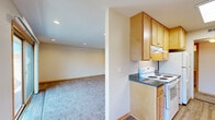 This single-floor unit offers a functional and comfortable layout with a clean, neutral aesthetic throughout. The galley-style kitchen is well-equipped, featuring light wood cabinetry, dark granite-style countertops, a double sink, a white electric range, a refrigerator, and durable wood-look flooring. A skylight adds brightness to this efficient cooking space. Adjacent to the kitchen, the open living and dining area is finished with plush carpet and recessed lighting, and flows seamlessly to a private balcony through a sliding glass door, providing views of the surrounding outdoor environment. A pendant chandelier marks the dining area, adding a subtle decorative touch. The bedrooms are carpeted and bright, each outfitted with a ceiling fan and light-framed windows that invite natural light and outdoor views. One bedroom features two windows and ample wall space, while another includes a closet and access to additional rooms. The bathrooms are finished with light wood vanities, solid-surface countertops, large mirrors, and tile flooring. Textured walls and warm wood trim details are consistent throughout the unit, contributing to a cohesive and inviting atmosphere. The overall layout, as seen in the floor plan, is efficiently organized for comfortable day-to-day living.