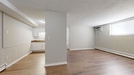 This single-floor unit is thoughtfully laid out to maximize functionality across its living spaces. Warm-toned hardwood-style flooring runs consistently throughout, lending a cohesive and clean aesthetic to every room. Neutral grey walls and white trim create a bright, understated backdrop, while textured ceilings add a classic character to the space.

The open living and dining area is defined by a partial dividing wall that separates it from the kitchen without fully enclosing the space, maintaining an open feel. A wall-mounted air conditioning unit and baseboard heating system ensure year-round climate control. One wall in the living area features distinctive white beadboard wainscoting, adding a subtle decorative detail.

The kitchen is well-equipped with white cabinetry, dark granite-style countertops, a subway tile backsplash, a stainless steel sink, and a white electric range with overhead cabinetry. Ample storage is provided through both upper and lower cabinet configurations.

The bedroom areas are generously sized, each featuring hardwood-style flooring and access to closet space, including at least one walk-in closet with built-in shelving. A hallway connects the private areas to the main living spaces, completing the practical and efficient floor plan.