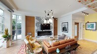 This single-floor space showcases a bold, eclectic interior design that blends color, pattern, and texture throughout. The main lounge area centers around a striking feature wall clad in geometric patterned tile, housing a linear fireplace and wall-mounted television, flanked by warm wood paneling. An eye-catching cluster pendant chandelier anchors the seating arrangement, which includes a substantial burnt-orange sectional sofa, mixed accent chairs, and vibrant patterned area rugs layered over parquet-style hardwood flooring.

Floor-to-ceiling windows and glass garage-style doors line one side of the space, inviting an abundance of natural light and offering direct views to an outdoor terrace. Exposed concrete columns add an industrial counterpoint to the decorative details throughout.

An entry gallery area features equally expressive design, with bold floral wallpaper extending across both walls and the coffered ceiling, complemented by a curated gallery of black-and-white framed photographs. A bar counter with upholstered stools provides a social focal point nearby. A dining area with a round table rounds out the layout, making this a multifunctional space designed for gathering, entertaining, and visual impact.