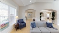 This thoughtfully designed single-floor space offers an open, airy layout that promotes easy movement and a warm sense of community. The main living area is anchored by soaring vaulted ceilings and elegant arched doorways that connect the various zones of the space, creating a seamless and inviting flow throughout. Large windows dressed with white blinds allow abundant natural light to fill the room, enhancing the bright, neutral color palette of soft whites and warm beige tones.

A standout feature of the living area is the classic fireplace framed by a crisp white mantle, flanked by large windows and topped with a wall-mounted television — making it an ideal gathering focal point. Comfortable seating, including plush sofas and accent chairs in coordinating blue tones, provides ample space for relaxation and socialization. Light-toned tile flooring runs consistently throughout, adding to the cohesive and clean aesthetic.

The kitchenette is well-appointed with rich warm-toned wood cabinetry, granite countertops, a stainless sink, and full-size black appliances including a refrigerator and microwave. Generous upper and lower cabinet storage ensures functional daily use. A decorative arched entry and wainscoting details throughout add refined architectural character to the overall space.