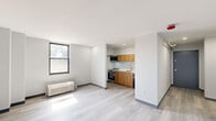 Located at 1930 Marion St in Columbia, SC, this one-bedroom, one-bathroom unit offers a clean, modern design across a single floor. The open living area features light wood-look luxury vinyl flooring, crisp white walls with dark baseboards, and a large black-framed window that brings in natural light and outdoor views. A wall-mounted PTAC unit provides individual climate control. The kitchen is efficiently integrated into the living space, equipped with warm wood-toned cabinetry, a stainless steel oven, a built-in microwave, a dishwasher, and a single-basin sink — all neatly arranged along one wall. The bedroom is a well-proportioned, private retreat with its own black-framed window, a baseboard heating unit, and recessed lighting. A dedicated closet area off the bedroom features built-in shelving and a hanging rod for organized storage. The bathroom is finished with neutral tile flooring, a white vanity with cabinet storage and a mirrored medicine cabinet, a standard toilet, and a shower/tub combination. Throughout the unit, the design emphasizes clean lines, neutral tones, and functional efficiency, making it a practical and comfortable living space.