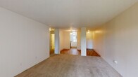 This single-floor residence accommodates four bedrooms, one bathroom, a kitchen, and a connecting hallway within a efficiently organized footprint. The open living area features a combination of hardwood flooring and wall-to-wall carpet, with a textured ceiling overhead. Structural columns define the transition between spaces, while a sliding glass door brings in natural light and provides views of surrounding greenery.

The bedrooms are carpeted and feature neutral walls, textured ceilings, and windows overlooking outdoor vegetation. Several bedrooms include sliding-door closets equipped with wire shelving systems and hanging rods, providing practical built-in storage. Baseboard heaters are present in multiple rooms. The primary bedroom offers a notably generous layout relative to the other bedrooms.

The kitchen is fitted with warm-toned wood cabinetry, light stone-finish countertops, a stainless steel sink, and an overhead range hood. The shared bathroom includes tile flooring in a neutral stone pattern, a wood vanity with an integrated sink, and a full bathtub with a shower. The hallway connects the bedroom wing to the main living areas, completing the straightforward and functional floor plan.