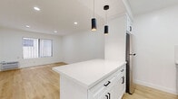 Located at 1776 N Sycamore Ave in the heart of Hollywood, Los Angeles, this thoughtfully designed single-floor unit offers a clean, modern aesthetic with high-quality finishes throughout. The open-concept kitchen and living area serves as the centerpiece of the space, featuring light hardwood flooring that runs seamlessly throughout and crisp white walls that maximize the sense of openness and brightness. The kitchen is equipped with full stainless steel appliances, including a gas range, over-the-range microwave, refrigerator, and dishwasher. White shaker-style cabinetry with matte black hardware pairs elegantly with a marble-veined quartz peninsula countertop, over which two sleek black cylindrical pendant lights hang as a stylish focal point. Recessed lighting and a window with vertical blinds provide ample illumination to the living area. A hallway connects the main living space to the bathroom and closet. The bathroom is well-appointed with marble-style tile surrounding a tub-shower combo enclosed by a sliding glass door with a black frame, complemented by matching black hardware accents. The dedicated closet offers practical storage, completing this well-organized and stylishly finished unit.