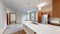 Located at 1868 N Astor St in Milwaukee, Wisconsin, this well-appointed one-bedroom, one-bathroom residence offers a thoughtfully designed single-floor layout. The open-concept kitchen is a standout feature, showcasing warm honey-toned cabinetry, a white quartz peninsula with an undermount sink, and a full suite of stainless steel appliances including a refrigerator, electric range, microwave, and dishwasher. Pendant lighting above the peninsula adds a modern touch, while durable hardwood-style flooring grounds the space with a clean, contemporary aesthetic. The living area flows naturally from the kitchen, offering a comfortable and versatile space bathed in natural light from multiple windows dressed with horizontal blinds. The generously sized bedroom features plush wall-to-wall carpeting, neutral tones, and dual windows that invite natural light while providing views of the surrounding neighborhood. A dedicated walk-in closet with wire shelving and hanging rods offers ample storage. The full bathroom is finished with warm wood-tone cabinetry, a white countertop vanity, hardwood-style flooring, and a shower-tub combination. Throughout the residence, warm wood door and window trim, neutral wall tones, and consistent finishes create a cohesive and welcoming atmosphere.