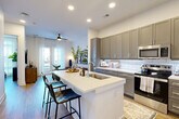 Located at 4015 South Blvd in Charlotte, NC, this well-appointed one-bedroom, one-bathroom residence offers a thoughtfully designed open-concept layout. The combined kitchen and living area serves as the heart of the home, featuring a large white quartz island with bar seating, gray shaker-style cabinetry, a white subway tile backsplash, and stainless steel appliances — all flowing seamlessly into a bright living space with wood-style flooring, recessed lighting, and a ceiling fan. Floor-to-ceiling glass doors flood the living area with natural light and open to a private patio. The bedroom is a serene retreat accented by large windows with sheer curtains that invite abundant daylight and outdoor views. A spacious walk-in closet with multi-tiered shelving and hanging rods provides generous storage. The full bathroom features a soaking tub with a tiled surround and direct access to the walk-in closet. A dedicated in-unit laundry area adds everyday convenience. Throughout the residence, light hardwood-style flooring and a clean, neutral color palette create a modern and cohesive aesthetic.
