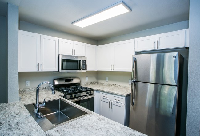 Fully equipped kitchen with stainless steel appliances, white shaker cabinets, and granite counters. - The Lido Apartments