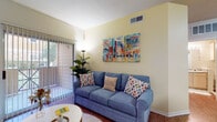 This well-appointed single-floor residence offers a thoughtfully designed layout that balances comfort and functionality across its key living areas. The living room serves as the heart of the home, featuring warm hardwood-style flooring, soft yellow walls, and a sliding glass door that fills the space with natural light and provides access to a private outdoor balcony. A vibrant Austin-themed art display adds a bold, local character to the room, while a built-in desk nook with open shelving creates a convenient workspace tucked neatly into the corner. The galley-style kitchen is efficiently laid out with countertops running along both sides, light wood cabinetry, granite-look countertops, and a full suite of appliances including an electric range, microwave, and dishwasher. Wood-look flooring continues through the kitchen for a cohesive feel. The bedroom is a restful retreat, highlighted by a rich olive green accent wall, plush carpeting, and a large window with sheer curtains that invite soft, diffused light. A spacious walk-in closet provides generous storage, and an en-suite bathroom is conveniently accessible from within the room. The full bathroom features a single vanity with ample cabinetry, a tub and shower combination, and classic tile surround, rounding out this inviting and functional space.