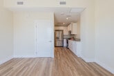 This single-floor unit offers a clean, modern design defined by warm hardwood-style flooring, crisp white trim, and soft neutral walls that create a bright and welcoming atmosphere throughout. The open living area is generously proportioned, bathed in natural light from a large window with blinds that frames a lush outdoor view. A flush ceiling light fixture adds a polished touch to the space.

The kitchen flows seamlessly from the living area and is thoughtfully designed with white shaker-style cabinetry extending to the ceiling, smooth light-toned countertops, and a full suite of stainless steel appliances, including a gas range, over-the-range microwave, refrigerator, and dishwasher. Recessed lighting illuminates the workspace, and a single-basin sink completes the functional layout.

The bathroom continues the home's clean aesthetic, featuring light wood-style flooring, a white vanity with an integrated sink, and a large mirror. A window fitted with slatted blinds allows natural light to filter in while maintaining privacy. A tankless water heater is neatly integrated into the space.

The entry area provides a welcoming threshold with access to an adjacent outdoor space, reinforcing the unit's bright, airy feel. Overall, the space presents a cohesive, contemporary design with quality finishes and a practical, comfortable layout.