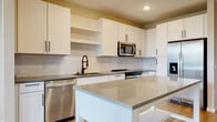 Located at 1015 Keymar Drive in Davenport, Florida, this single-story unit presents a clean, modern aesthetic with consistent design choices carried throughout every room. The open-concept layout connects the kitchen and living areas seamlessly, with light wood-look flooring underfoot that enhances the bright, airy atmosphere.

The kitchen is a standout feature, equipped with white shaker-style cabinetry, gray quartz countertops, a white subway tile backsplash, and a full suite of stainless steel appliances including a refrigerator with ice maker, range, microwave, and dishwasher. A mobile island with a matching quartz surface provides additional prep space and flexibility. Matte black hardware and fixtures add a contemporary contrast throughout.

The living area is generously proportioned, benefiting from natural light through large windows and a ceiling fan. Built-in shelving adds functional detail to the space. Bedrooms feature plush carpeting, ceiling fans, and wide windows that invite outdoor views and natural light. The walk-in closet includes multi-tier wire shelving for organized storage.

The bathroom is well-appointed with a dual-sink vanity, gray quartz countertops, white cabinetry, framed mirrors, and wood-look flooring. An in-unit laundry area completes the practical offerings of this well-designed space.