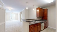 Located at 1001 Hayes Ln in Holly Springs, NC, this well-appointed one-bedroom, one-bathroom residence offers a thoughtfully designed single-level layout. The open-concept living, dining, and kitchen area forms the heart of the home, creating a seamless and functional shared space. The kitchen is equipped with rich, warm-toned cabinetry, dark granite-style countertops, a tile backsplash, stainless steel appliances including a refrigerator, range, and built-in microwave, and a peninsula with a double sink and pendant lighting overhead — ideal for casual dining and entertaining. Soft, neutral-toned carpeting flows throughout the living areas and bedroom, complemented by light tile flooring in the kitchen. Crown molding and ceiling fans with light fixtures are present throughout, adding a polished finish. The spacious bedroom features a ceiling fan, natural light from large windows with views of surrounding greenery, and access to two closets for ample storage. The bathroom is highlighted by a large soaking tub with tiled surround and built-in shelving. A dedicated laundry area adds everyday convenience. The overall palette of warm beige tones and clean white trim creates a bright, neutral, and welcoming ambiance throughout.
