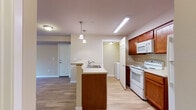 Located at 3105 East Assembly Road in Spokane, WA, unit C202 is a well-appointed single-floor residence designed for comfortable everyday living. The open living area features warm hardwood-style flooring, neutral beige walls, and a glass-paneled door that leads to a private balcony overlooking lush greenery. A wall-mounted HVAC unit and floor vents ensure year-round climate control. The kitchen is a standout feature, highlighted by rich warm-toned wood cabinetry, light countertops, and a peninsula with pendant lighting and a double-basin sink. White appliances, including a range and microwave, are neatly integrated alongside ample upper and lower cabinet storage. Adjacent to the kitchen, a dedicated laundry area accommodates a full-size washer and dryer. The bedroom is carpeted for comfort, receives natural light through a large window with balcony access, and includes a utility closet. The bathroom features wood-tone cabinetry, a baseboard heater, and a full soaking tub with shower. Throughout, consistent light flooring, clean white trim, and a cohesive neutral palette create a bright, functional, and inviting atmosphere.