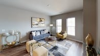 This thoughtfully designed single-floor residence offers a cohesive contemporary aesthetic accented by a warm palette of gray, white, and gold tones throughout. The open-concept kitchen is equipped with stainless steel and black appliances, including a full-size refrigerator, electric range, and built-in microwave. Dark cabinetry is paired with light quartz countertops and a double stainless steel sink, while white upper cabinets and stylish pendant lighting add visual contrast. Wood-look flooring flows through the kitchen and living areas, lending warmth and continuity. The living room is bright and welcoming, featuring large windows that invite natural light and provide a comfortable area for relaxing or entertaining. A dedicated workspace nook with a sleek white desk and natural light offers a functional area for productivity. The bedrooms feature plush carpeting, ceiling fans, and windows with blinds, creating restful retreats. One bedroom also includes a compact desk area. Both bathrooms are finished with dark vanity cabinetry, white countertops, and a tub-shower combination. The unit's consistent design language — neutral walls, gold accents, and modern fixtures — creates a polished and livable environment throughout.