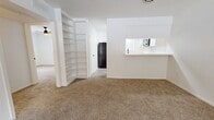 This 850-square-foot apartment at 3411 Cummins Street in Houston, TX offers a single-floor layout with 2 bedrooms and 2 bathrooms. The carpeted living room features a textured ceiling, ceiling fan, and a pass-through opening to the galley-style kitchen, which is equipped with black appliances, white cabinetry, and light wood-look vinyl flooring. Both bedrooms include ceiling fans, carpet flooring, and windows with vertical blinds. The 220-square-foot primary bedroom features a closet with mirrored sliding doors. One bathroom includes a white vanity with black fixtures and vinyl flooring, while the second bathroom features a tiled tub-shower combination with vinyl flooring. A hallway connects all rooms throughout the unit.
