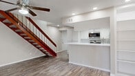 This two-story home offers 2 bedrooms and 3 bathrooms across a well-organized layout, with the majority of the living space situated on the main floor. Wood-look flooring runs throughout both levels, providing a cohesive and easy-to-maintain aesthetic.

The main floor centers around an open-concept living and kitchen area. The kitchen features white cabinetry, a white quartz peninsula with an integrated sink, a tile backsplash, and stainless steel appliances including a refrigerator, range, and built-in microwave. A set of built-in shelving units adds functional display space nearby. The adjacent living room is highlighted by a full wood-paneled accent wall with a fireplace, a ceiling fan, and sliding glass doors that invite natural light. A bold wood-and-metal staircase serves as a visual focal point connecting both floors.

The upper level houses the bedrooms, including a generously sized primary bedroom with a ceiling fan, a large window with views of the surrounding greenery, and a mirrored sliding-door closet. The bathrooms are finished with white quartz countertops, white cabinetry, and tub-shower combinations. Two hallways and two closets provide ample storage throughout. Textured ceilings and recessed lighting complete the interior character of this functional, well-appointed home.