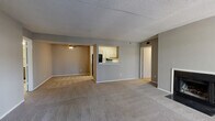 This single-floor residence offers a well-organized layout across three bedrooms, two bathrooms, a combined kitchen and living area, two closets, and a connecting hallway. The open-concept living and dining space is a central feature, highlighted by a wood-burning fireplace, neutral carpeting, and a textured ceiling. A ceiling fan adds practical comfort, while a large window brings in natural light and connects the interior to the outdoors.

The kitchen is designed as a galley-style space, accessible via a pass-through opening to the living area. It features gray cabinetry, a white countertop, a black refrigerator, and a range, with a louvered door providing additional access or storage.

The primary bedroom is a well-proportioned retreat with two windows that allow ample natural light. It includes access to a walk-in closet equipped with dual shelving rails on both sides, offering generous storage capacity. The additional bedrooms are carpeted and feature neutral gray walls with textured ceilings.

The bathrooms include updated vanities with white countertops, modern hardware, and wood-look flooring. Throughout the residence, a consistent neutral color palette of gray and beige tones creates a cohesive and understated aesthetic.