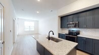 This single-floor residence in Lenexa, Kansas, near I-435 N, presents a cohesive modern design characterized by clean lines, neutral tones, and quality finishes. The kitchen serves as a standout feature, equipped with bold slate-blue cabinetry extending to the ceiling, stainless steel appliances, a white subway tile backsplash, and granite countertops. A central island with an undermount sink and a matte black faucet provides additional prep space while connecting seamlessly to the open living and dining areas. Light wood-look flooring flows throughout the main living spaces, enhancing the bright, airy atmosphere created by recessed lighting and natural light from well-placed windows. The living area offers an open, versatile layout with direct sightlines to the kitchen. Bedrooms feature plush carpeting, ceiling fans, and windows with blinds for natural light and privacy. The bathroom is finished with a navy vanity topped with a granite countertop, a backlit mirror, wood-look flooring, and a glass-enclosed walk-in shower with tiled walls and a built-in bench, delivering a polished, contemporary aesthetic throughout.