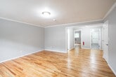 Located at 645 Belle Terre Rd in Port Jefferson, NY, this single-floor residence offers a clean, well-maintained interior with a cohesive design throughout. Warm hardwood flooring extends across the living areas and bedrooms, complemented by crisp white crown molding and soft gray walls that create a bright, neutral aesthetic.

The open living area provides a comfortable sense of space, with flush ceiling lighting and baseboard heating visible throughout. Multiple rooms feature sliding closet doors and windows that invite natural light and outdoor greenery views, with window-unit air conditioning available for warm-weather comfort.

The galley-style kitchen is a functional highlight, featuring white cabinetry on both sides, granite-patterned countertops, a stainless steel sink, a white electric range with overhead ventilation, and a full-size refrigerator. Light wood-tone flooring in the kitchen complements the overall palette, and the layout flows directly into the main living corridor.

The bathroom is finished with large-format marble-look wall tiles surrounding a full soaking tub and shower combination, paired with chrome fixtures for a clean, timeless look. The floorplan, as seen in the dollhouse view, presents a compact yet efficient layout with well-defined room separations, making this a practical and polished single-level residence in the Port Jefferson area.