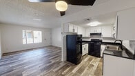This single-floor residence offers a thoughtfully updated interior with a cohesive, modern aesthetic throughout. The kitchen serves as a functional centerpiece, featuring crisp white shaker cabinetry with matte black hardware, dark granite-style countertops, a herringbone tile backsplash, a stainless steel sink, and black appliances including a range and refrigerator. Wood-look plank flooring runs through the kitchen and main living areas, adding warmth and durability to the space.

The open living and dining areas are bright and airy, benefiting from natural light through large windows dressed with horizontal blinds. A ceiling fan with a built-in light fixture adds both comfort and function to the main living space. The layout flows naturally between rooms, with a partial wall divider providing subtle separation without closing off the open feel.

The bedrooms feature soft, neutral-toned carpet and generous windows that allow natural light to fill each room. White walls and clean trim throughout maintain a fresh, move-in-ready appearance.

The bathroom is cleanly finished with a white vanity cabinet, dark granite-topped counters, a framed mirror with overhead lighting, matte black fixtures, and a full tub and shower combination. Wood-look flooring extends into the bathroom, tying the space together with the rest of the home's consistent design language.