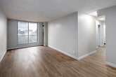 Located on the 10th floor at 100 Ferguson Ave S in Hamilton, Ontario, this two-bedroom, one-bathroom unit offers a functional and modern layout finished with consistent light-toned vinyl plank flooring throughout. The living area is bright and open, featuring a large sliding glass door that frames sweeping views of the Hamilton skyline, filling the space with natural light. The kitchen is efficiently designed in a galley configuration, outfitted with white cabinetry featuring black hardware, stone-look countertops, a undermount sink with a brushed nickel faucet, a tile backsplash, and stainless steel appliances including a dishwasher and refrigerator. The primary bedroom offers a comfortable footprint with a large sliding glass door providing additional city views and natural light. The second bedroom features a built-in sliding-door closet and connects to the hallway, making it versatile for various uses. The bathroom is finished in a clean, contemporary style with a white vanity, square undermount sink, chrome fixtures, a large mirror with vanity lighting, and a glass mosaic tile accent wall. Neutral wall tones and clean white trim unify the space throughout, lending it a crisp and modern ambiance well-suited to urban living.