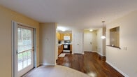 This single-floor residence offers a functional and comfortable open-concept layout, thoughtfully designed to maximize both space and livability. Rich, dark hardwood flooring flows through the main living and kitchen areas, creating a warm and cohesive aesthetic throughout.

The kitchen is well-appointed with warm oak cabinetry offering generous storage, light-toned countertops, a double stainless steel sink positioned beneath a window with outdoor greenery views, and a full suite of appliances including a gas range, over-the-range microwave, refrigerator, and dishwasher. A pendant light fixture adds a finishing touch to the dining area nearby.

The open living area transitions seamlessly from the kitchen, featuring soft carpeting and multiple windows that invite natural light and provide pleasant views of the surrounding greenery. A dedicated entryway with a paneled door and pendant lighting completes the main living zone.

The bedroom is carpeted and quietly tucked away, featuring a window that frames outdoor foliage and provides a peaceful, naturally lit retreat.

The bathroom is clean and practical, featuring tile flooring, a single-sink vanity with oak cabinetry, a medicine cabinet with vanity lighting, and a shower-tub combination with a curtain. Grab bars are also present, adding an accessibility-conscious detail to the space.