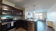 Located at 1411 E 105th St in Cleveland, Ohio, this well-appointed single-floor residential unit offers a thoughtfully designed open-concept layout that seamlessly connects the kitchen, dining, and living areas. The kitchen is a standout feature, showcasing rich dark-espresso cabinetry, granite countertops, a subway tile backsplash, and a full suite of stainless steel appliances including a range, over-the-range microwave, dishwasher, and refrigerator. Pendant lighting above the peninsula adds a polished touch, while wood-look flooring runs throughout the main living areas, adding warmth and continuity.

The living space is bright and inviting, with large windows offering views of the surrounding treeline, allowing generous natural light to fill the room. A dedicated dining nook with oversized windows further enhances the airy feel of the space.

Both bedrooms are comfortably sized, each featuring natural light from well-placed windows and wood-look flooring. The bathroom is designed with dual vanities, granite countertops, and matching dark cabinetry, providing ample storage and a cohesive aesthetic that ties the entire unit together.