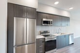 Located at 201 North La Brea Avenue in Inglewood, CA, this thoughtfully designed single-floor unit offers a clean, modern aesthetic throughout. Light-toned wood-look flooring runs continuously across the space, complementing the neutral warm-white walls and creating a cohesive, contemporary feel.

The kitchen is a standout feature, equipped with full-size stainless steel appliances including a French door refrigerator, electric range with over-the-range microwave, and dishwasher. Two-tone cabinetry — dark wood-grain lowers paired with muted blue-gray uppers — frames a light-colored countertop and a classic tile backsplash, delivering both style and function.

The two living areas provide flexible use of space. One opens to a balcony with large windows that invite natural light and urban views, while the other offers a more intimate setting. The hallway connects the main areas efficiently and includes access to a stacked in-unit washer and dryer tucked neatly behind louvered doors.

The bathroom features a clean, minimalist design with wood-look tile flooring, white walls, and chrome grab bars, reflecting an accessibility-conscious layout. Recessed lighting throughout the unit ensures consistent, well-distributed illumination across every room. The overall design emphasizes modern simplicity, practical functionality, and comfortable everyday living.