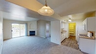 This single-floor residence offers a functional and comfortable layout designed for everyday living. The open living area is anchored by a fireplace with a classic tile surround and features vaulted ceilings with a decorative arched niche, adding architectural character to the space. A pendant light fixture hangs above the transition to the kitchen, and sliding glass doors lead to a private balcony, filling the room with natural light. The kitchen is designed for efficiency, with white cabinetry, laminate countertops, wood-look flooring, and a full-size refrigerator. A generous walk-in pantry with open shelving provides ample storage. Adjacent to the kitchen, a dedicated laundry room houses a full-size washer and dryer beneath additional upper cabinetry. The residence includes multiple bedrooms, each finished with plush carpeting and windows that invite natural light. The primary bedroom features a walk-in closet and access to a private bathroom. A second bathroom includes a shower-tub combination and wood-look flooring. Throughout the unit, the neutral color palette and clean finishes create a bright, cohesive ambiance well-suited for comfortable, practical living.