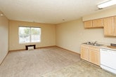 This single-floor unit offers a practical and well-organized layout designed for comfortable living. The kitchen is fully equipped with light wood cabinetry, ample upper and lower storage, a double-basin sink, white appliances including a range, microwave, dishwasher, and refrigerator, and durable tile flooring. The open living and dining area flows seamlessly from the kitchen, featuring soft carpeting, neutral warm-toned walls, and a large window that brings in natural light. Additional doors in the living area provide access to entry points and hallways, keeping the floor plan connected and easy to navigate. The bedrooms are carpeted and feature neutral walls, textured ceilings, and windows that allow for natural light and outside views. One bedroom includes a spacious walk-in closet outfitted with white wire shelving and a hanging rod, offering generous storage capacity. The bathroom is clean and functional, featuring tile flooring, a walk-in shower with a curtain rod, a toilet, and a vanity. Throughout the unit, wood baseboards, textured ceilings, and a consistent neutral color palette create a cohesive and understated aesthetic.