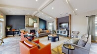 Located at 11602 Apex View Dr in Louisville, KY, this single-story community clubhouse is a thoughtfully designed gathering space that blends rustic charm with contemporary style. The centerpiece of the space is a spacious lounge area anchored by a floor-to-ceiling stacked stone fireplace and dramatic vaulted ceilings accented with exposed beam detailing. Bold navy and slate accent walls contrast beautifully with reclaimed wood columns, while the striking herringbone-patterned hardwood flooring runs throughout, adding warmth and visual interest. Comfortable seating arrangements, including rich leather chairs and upholstered sofas, create an inviting atmosphere for socializing. A built-in media wall provides an entertainment focal point. The business center offers dual workstations with built-in cabinetry and stylish pendant lighting, ideal for productivity. A casual dining area features high-top tables and bar-height seating bathed in natural light from large windows and French doors that open to an outdoor patio. The wet bar area is equipped with granite countertops, white cabinetry, and a stainless undermount sink, complemented by a bold typographic mural that serves as a striking artistic statement. Together, these spaces create a vibrant, amenity-rich environment designed for both work and leisure.
