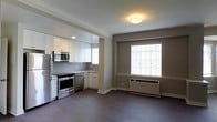 Located at 5500 Wissahickon Ave in Philadelphia's 19144 zip code, this single-floor space offers a well-designed open-concept layout that seamlessly connects the kitchen and living area. The kitchen is outfitted with stainless steel appliances, including a gas range, microwave, and dishwasher, complemented by crisp white cabinetry, a subway tile backsplash, and ample counter space. Crown molding details add a refined architectural touch throughout the space. The living area is bathed in natural light courtesy of large windows fitted with white blinds, creating a bright and welcoming atmosphere. Warm-toned walls contrast with the white trim and dark hardwood-style flooring, lending the space a balanced, contemporary aesthetic. A wall-mounted HVAC unit ensures year-round climate control. Recessed and flush-mount ceiling lighting provide consistent illumination throughout. The overall design is clean and functional, offering a comfortable and move-in-ready environment well-suited for everyday living.