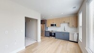 Located at 2902 N Arthur Ashe Blvd in Richmond, VA, this thoughtfully designed one-bedroom, one-bathroom residence offers a modern aesthetic throughout its efficiently laid-out single floor. The open living and kitchen area is anchored by light hardwood flooring and a contemporary kitchen featuring two-tone cabinetry — cool grey lower cabinets paired with warm natural wood uppers — complemented by white subway tile backsplash, gold hardware accents, and a full suite of stainless steel appliances including a range, microwave, refrigerator, and dishwasher. Recessed lighting illuminates the space cleanly. A bright hallway with dark-paneled doors and crisp white trim connects the main living area to the private quarters. The bedroom is finished with plush carpet, a ceiling fan, and a standout dark barn-style sliding door that opens to the living space, adding a striking architectural detail. The bathroom offers a clean, spa-like feel with light hardwood flooring, a tub-shower combination adorned with white tile and matte black fixtures, a dark vanity with gold hardware, and built-in open shelving leading into a dedicated closet with ample storage. The overall palette of whites, naturals, and muted tones creates a calm, cohesive atmosphere throughout.