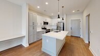 Located at 400 Universal Rd in Southern Pines, NC, this single-story 2-bedroom, 1-bathroom home offers a thoughtfully designed layout with clean, contemporary finishes throughout. Warm hardwood-style flooring flows consistently across all rooms, creating a cohesive and inviting atmosphere.

The kitchen serves as a standout centerpiece, featuring shaker-style cabinetry in soft grey and white tones, stainless steel appliances including a refrigerator, range, and built-in microwave, white quartz countertops, a deep undermount sink, and a large center island with pendant lighting — ideal for both meal prep and casual dining.

The living and dining areas are open and airy, with arched doorway details, ceiling fans, and natural light filtering in through window blinds. The primary bedroom is generously sized, offering ample space and direct access to a walk-in closet outfitted with wire shelving systems for organized storage.

The bathroom is finished with a glass-panel shower featuring matte black hardware and a built-in grab bar. A dedicated laundry room includes a top-load washer, wire shelving, and an electrical panel access point. A hallway connects all areas efficiently, completing this functional and modern single-floor layout.