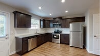 This two-story home in Clarksville, Tennessee offers a well-designed layout across two floors. The kitchen serves as a standout feature, showcasing rich dark-wood cabinetry, granite countertops, a classic subway tile backsplash, and a full suite of stainless steel appliances including a dishwasher, electric range with over-the-range microwave, and refrigerator. Recessed lighting and warm hardwood-style flooring complete the space, creating a functional and stylish cooking environment. A convenient half-bath on the lower level features hardwood-style flooring and clean, neutral finishes. The upper floor houses the two bedrooms, each with plush carpeting and natural light from windows with blinds. One bedroom includes a ceiling fan, while the other features a walk-in closet with built-in shelving. The full bathroom upstairs is appointed with stone-look tile flooring, a dark vanity with a white countertop, and a tub-shower combination. A dedicated laundry area with a full-size washer and dryer adds everyday convenience. Throughout the home, neutral wall tones, white trim, and consistent finishes create a cohesive and move-in-ready atmosphere.