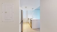 Located at 625 Avenue de l'Équinoxe in Brossard, this modern one-bedroom, one-bathroom unit offers a thoughtfully designed layout with contemporary finishes throughout. The open-concept living and kitchen area forms the heart of the space, anchored by a striking quartz waterfall island with an undermount sink and pendant lighting. The kitchen is equipped with stainless steel appliances, two-tone cabinetry combining white upper cabinets with warm wood lower units, and clean white tile backsplash. Light-toned hardwood flooring runs throughout, complementing the exposed concrete ceiling that adds an industrial character to the modern interior. The living area features a wall-mounted air conditioning unit and a built-in entryway nook with wood shelving and seating. Large sliding glass doors and windows flood the space with natural light while offering open views of the surrounding urban skyline. The bedroom is a comfortable, bright room with its own window framing city views, exposed concrete ceiling details, and access to a dedicated closet with built-in shelving. The bathroom is finished with large-format beige floor tiles, a floating wood vanity with a stone countertop, a mirrored medicine cabinet, and a frameless glass sliding shower enclosure. A stacked washer and dryer unit is also included within the unit.