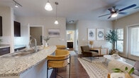 This well-appointed one-bedroom, one-bathroom residence in Austin, TX offers an efficient and thoughtfully designed single-level layout. The open-concept kitchen and living area serves as the heart of the home, featuring rich dark cabinetry, granite countertops, a central island with a built-in sink, pendant and track lighting, and a full suite of stainless steel appliances. The island accommodates bar seating, making it ideal for casual dining or entertaining. Hardwood-style flooring runs throughout the main living areas, adding warmth and continuity to the space. The living room is bright and inviting, with direct access to an outdoor area through a glass-paneled door flanked by windows that invite natural light and outdoor views. A ceiling fan adds comfort overhead. The bedroom is a calm retreat, highlighted by a distinctive blue accent wall, plush carpeting, and multiple windows overlooking greenery. A dedicated closet provides organized storage. The bathroom features matching dark cabinetry, a tub-shower combination, and direct access to the walk-in closet, streamlining the daily routine. The overall ambiance is modern yet comfortable, with neutral tones and clean finishes throughout.