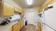 This single-floor residence offers a well-organized layout with distinct living, dining, kitchen, and sleeping areas. The galley-style kitchen is efficiently designed with light oak cabinetry lining both walls, providing ample upper and lower storage. A double-basin sink, white appliances including a coil-top range and dishwasher, and grey laminate countertops complete the functional workspace. A closeted storage area is accessible directly from the kitchen. A half-wall breakfast bar separates the kitchen from the adjacent dining and living areas, creating an open, connected feel. The entry door opens conveniently into this shared space.

The living room features neutral-toned carpet, a ceiling fan with light fixture, and windows that allow natural light to brighten the room. The bedrooms are carpeted and each include sliding closet doors, with windows providing additional natural light. The full bathroom is equipped with a dual-sink vanity topped with speckled countertops, light oak cabinetry, a large wall mirror, and wood-look flooring, with a shower-tub combination. Throughout the unit, warm neutral tones and wood-look flooring in key areas contribute to a cohesive, comfortable ambiance.
