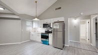 Located at 8014 Tommy Ct in Tampa, Florida, this single-story home showcases a thoughtfully updated interior with a clean, modern aesthetic. The open-concept living area is anchored by soaring vaulted ceilings and recessed lighting, creating a bright and airy atmosphere. Light gray luxury vinyl plank flooring extends throughout the entire home, providing a cohesive and contemporary look.

The kitchen is well-appointed with white shaker-style cabinetry, granite countertops, and a classic white subway tile backsplash. A suite of stainless steel appliances — including a refrigerator, electric range, and over-the-range microwave — equips the space for everyday cooking. A pendant light fixture with a brass finish adds a subtle decorative touch above the kitchen area.

The bedrooms are generously sized, each featuring vaulted or elevated ceilings, neutral gray walls, and ample natural light from windows with blinds. One bedroom includes a closet with built-in shelving, offering practical storage. The bathroom is clean and functional, featuring light gray walls, vinyl plank flooring, a white vanity, and a full tub/shower combination. Throughout the home, crisp white trim and baseboards provide a polished finishing detail.