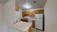 This single-story unit offers a practical and straightforward layout designed for comfortable everyday living. The kitchen is a standout functional space, equipped with warm oak cabinetry providing ample upper and lower storage, light-toned countertops, and a full suite of white appliances including a coil-top electric range, dishwasher, and refrigerator. A double-basin sink is positioned along the counter run, and a peninsula extends outward, creating additional prep space and a natural transition into the adjacent living area. Tile flooring runs throughout the kitchen, while textured ceilings are consistent across the unit.

The living area is open and carpeted, offering a clean, neutral canvas with beige walls and white baseboards. A ceiling fan with a light fixture provides overhead illumination, and a window along one wall brings in natural light with views of surrounding greenery. A front entry door with an adjacent window further brightens the space.

The bedroom is generously sized, also carpeted, with a ceiling fan, a window overlooking outdoor greenery, and ample wall space. The bathroom includes a wood-toned vanity with a light countertop, tile flooring, and a notable convenience — a stacked in-unit washer and dryer tucked neatly into the space.