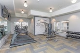 The Midtown Pointe Fitness & Wellness Center at 4590 N Campbell Rd in Royal Oak, Michigan, is a thoughtfully designed, single-floor facility dedicated to health and fitness. The space is bright and welcoming, with large windows throughout that allow abundant natural light to fill the room and provide views of the surrounding neighborhood.

The flooring features a stylish herringbone-patterned carpet tile in neutral tones, lending a modern aesthetic throughout. A bold accent wall adorned with motivational typography — including the words "Fitness," "Wellness," "motivate," "inspire," "believe," and "Dedication" — sets an energizing tone upon entry.

The cardio zone is well-appointed with a row of TRUE-brand treadmills, elliptical trainers, a stair climber, and an interactive cycling bike, complemented by wall-mounted flat-screen televisions. The strength training area includes a multi-station cable and weight machine, an adjustable bench, and a tiered dumbbell rack with a full selection of free weights.

A dedicated functional fitness section houses stability balls, medicine balls on a rack, resistance tools, and additional cardio equipment, offering a versatile space for cross-training and recovery workouts. Full-length mirrors along one wall enhance the sense of openness and allow for form monitoring during exercise.

The overall ambiance is clean, modern, and motivating — a comprehensive fitness destination designed to serve a wide range of workout needs.