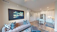Located in Orlando's vibrant Ivanhoe Village neighborhood, this thoughtfully designed one-bedroom, two-bathroom residence offers a modern open-concept layout that maximizes every inch of its well-appointed floor plan. Rich wood-look flooring flows throughout the main living areas, tying the spaces together seamlessly.

The kitchen is a standout feature, outfitted with crisp white cabinetry, a marble-style tile backsplash, stainless steel appliances including a French-door refrigerator, and generous counter space. A movable island with a neutral countertop provides additional prep space and casual seating.

The living room is bright and welcoming, anchored by a ceiling fan and floor-to-ceiling glass doors that open to a private balcony with outdoor views. Recessed lighting and neutral wall tones create a clean, contemporary ambiance throughout.

The bedroom offers a cozy retreat with carpeted flooring, a large window with outdoor views, and dedicated closet space. The primary bathroom features wood-look tile flooring, a glass-enclosed walk-in shower with white subway tile, and a white vanity with ample storage. A second full bathroom adds convenience for guests.

The dedicated entrance and closet round out this efficiently designed single-floor residence, ideal for comfortable urban living.