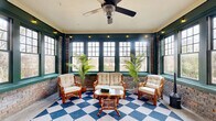 Located at 1508 Madison Ave in Memphis, Tennessee, this sunroom is a characterful and inviting retreat that masterfully blends rustic and classic design elements. The space is defined by its exposed brick walls, which lend warmth and historic character throughout. Bold, deep green window trim frames an expansive array of multi-pane windows on multiple walls, flooding the interior with abundant natural light and offering open views of the surrounding outdoor scenery.

The eye-catching blue-and-white checkered floor serves as a striking focal point, adding a playful yet timeless aesthetic to the room. Crown molding lines the ceiling, contributing a refined architectural detail, while a ceiling fan with a decorative light fixture provides both comfort and ambiance. String lights are strung along the upper trim, adding a warm, inviting glow.

The space is divided into two distinct seating zones: one featuring a rattan loveseat, matching armchairs, and a rattan coffee table arranged atop the patterned rug, and another more intimate area with a wrought iron bistro table and chairs set near an ornate glass-paneled entry door. Tall potted palms punctuate the space, enhancing its bright, airy atmosphere. A small wood-burning stove adds a cozy, functional touch, making this sunroom a versatile and welcoming space year-round.