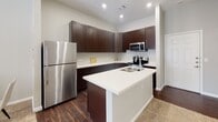 This single-floor residence at 2301 N Frazier St in Conroe, Texas offers a well-designed, functional layout with modern finishes throughout. The kitchen is a standout feature, showcasing rich dark espresso cabinetry, crisp white quartz countertops, a peninsula island with a sink, and a full suite of stainless steel appliances including a refrigerator, electric range, and built-in microwave. Dark wood-look flooring adds warmth and continuity to the kitchen area. The living room is bright and inviting, with soaring ceilings and a set of French doors that flood the space with natural light and provide access to an outdoor area, creating a seamless indoor-outdoor connection. The bedroom is generously sized and carpeted for comfort, featuring multiple windows dressed with blinds and a ceiling fan overhead. It connects to a long, well-appointed en suite bathroom with dark cabinetry, dual sinks, white countertops, and dark wood-look flooring. A walk-in closet with multi-tier shelving and hanging rods offers ample storage. The overall design palette of soft gray walls, white trim, and contrasting dark finishes creates a cohesive, contemporary aesthetic throughout the home.