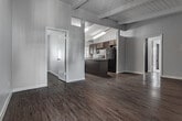 Located at 1730 Rogers Pl in Burbank, CA, this single-story unit offers a well-designed layout with a cohesive blend of functionality and character. The open-concept living and dining area is defined by striking exposed beam ceilings with white shiplap detailing, complemented by rich, dark hardwood-style flooring that runs throughout the main living spaces. The kitchen is a standout feature, offering generous counter space with speckled laminate countertops, a large central island, dark espresso cabinetry with a built-in wine rack, black appliances including a gas range and refrigerator, and a double-basin sink beneath a window that brings in natural light. Vertical blinds throughout the unit provide privacy while allowing light to filter in. The bedroom is carpeted for comfort and features exposed beam ceilings consistent with the rest of the home, along with an open closet with built-in shelving. Two bathrooms serve the unit — one with a full tub/shower combo, a single vanity with a large mirror, and a frosted window, and a second with a white vanity and mirror. The overall palette of cool grey walls and white trim creates a clean, neutral aesthetic throughout.