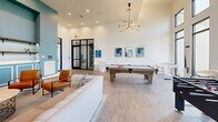 Located at 8890 Ransley Station Blvd in Pensacola, Florida, this single-floor community amenity space is thoughtfully designed for both relaxation and recreation. The open-concept layout is anchored by dramatic soaring ceilings that amplify the sense of spaciousness throughout. Crisp white walls are complemented by vibrant teal accent walls, creating a contemporary and inviting atmosphere.

The space is generously appointed with entertainment options, including a full-size pool table at its center and a foosball table positioned near a wall of tall, floor-to-ceiling windows that flood the room with natural light and offer views of the surrounding greenery and community grounds. A large-format connect-four game adds a playful touch to the gaming area.

The lounge area features a plush neutral sofa, leather accent chairs, and a stylish sputnik chandelier overhead. A wall-mounted flat-screen television, built-in cabinetry, decorative shelving, and wainscoting details on the teal feature wall add refined character to the space. The dining nook, set directly against expansive windows, provides an intimate seating area with views of the landscaped exterior. Light wood-toned tile flooring runs throughout, tying the space together with a clean, modern aesthetic ideal for community gatherings.