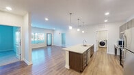 Located at 15 W La Quinta Ct in Rogers, Arkansas, this single-floor unit presents a clean, modern design characterized by an open-concept layout and consistent use of quality finishes throughout. The living area is generously proportioned, featuring warm wood-look flooring, recessed lighting, and large windows that invite abundant natural light while offering views of the surrounding exterior. The space flows seamlessly into the kitchen and dining area, creating an inviting and functional environment.

The kitchen is a standout feature, equipped with dark espresso-toned cabinetry, granite countertops, a white subway tile backsplash, and a full suite of stainless steel appliances including a range, refrigerator, and dishwasher. A central island with an undermount sink and pendant lighting above adds both workspace and visual appeal.

A dedicated laundry room houses a full-size washer and dryer alongside wire shelving for added storage. The bedroom offers plush carpeting, a ceiling fan, and a window with natural light. The bathroom is appointed with granite vanity counters, dark cabinetry, wood-look flooring, and a full tub-shower combination. Throughout the unit, crisp white walls and cohesive finishes contribute to a bright, contemporary ambiance.