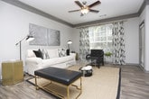 Located in Sandy Springs, GA, this single-floor residence offers a well-designed layout with a cohesive, contemporary aesthetic throughout. The kitchen is a standout feature, showcasing light gray cabinetry, stainless steel appliances, and an expansive granite-topped peninsula with an undermount sink and pendant lighting — ideal for both cooking and casual dining. Wood-look flooring flows through the main living areas, complemented by crown molding that adds a refined architectural touch.

The living room is generously proportioned, featuring a ceiling fan, large windows with natural light, and ample space for comfortable seating arrangements. A dedicated entryway or transitional nook features hardwood-style flooring and crown molding detailing, providing an elegant introduction to the home.

The primary bedroom is bathed in natural light from large windows dressed with sheer curtains and blinds, with plush carpet underfoot. A second bedroom also features carpet and a well-appointed layout. A flexible third room, finished with wood-look flooring and a walk-in closet, functions equally well as a bedroom, office, or studio space with natural light from a window. The bathroom includes a full soaking tub with tile surround. Throughout, neutral gray tones and modern fixtures create a clean, inviting atmosphere.